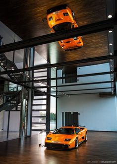 two orange sports cars parked in front of a glass building with staircases and windows