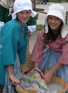 three women in dresses and bonnets are holding a basket full of clothes while smiling at the camera