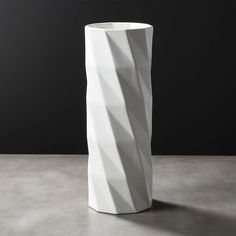 a tall white vase sitting on top of a cement floor next to a black wall