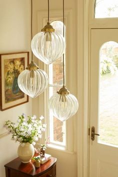 three glass globes hanging from the ceiling above a table with flowers and vase on it