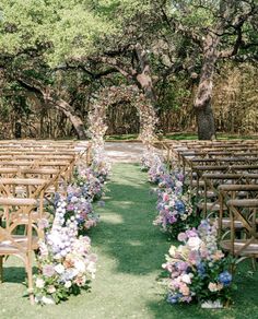 an outdoor ceremony set up with wooden chairs and floral arrangements on the aisle, surrounded by trees