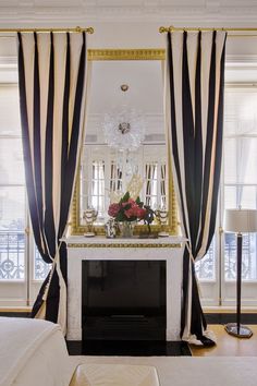 a living room with black and white drapes on the window sill, fireplace mantel, and chandelier