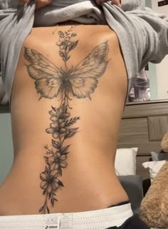 the back of a woman's stomach with flowers and a butterfly tattoo on it