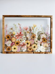 a wooden frame filled with flowers on top of a white table next to a wall