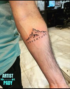 a man's arm with the words adventure on it and a mountain behind him