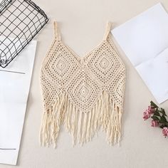 a crocheted top with tassels and flowers on the table next to it