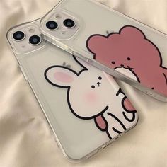 two cell phones are sitting next to each other on a white sheet with a pink bear