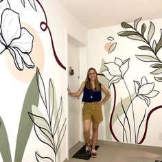 a woman standing next to a wall with flowers painted on it