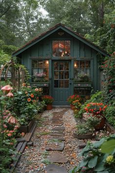 a small green shed with lots of flowers in the front and windows on each side