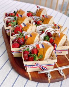 small trays filled with sandwiches and strawberries on top of a wooden platter