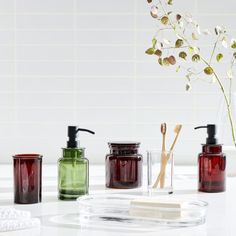 three different colored glass containers with soap and toothbrushes on a white countertop