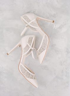 a pair of white high heeled shoes on top of a marble floor with crystals