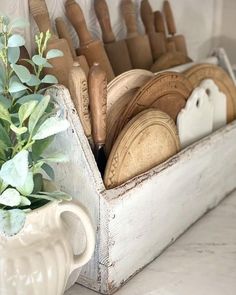 a white vase filled with wooden utensils on top of a counter next to a potted plant