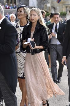 two women in dresses and hats are walking down the street with other people behind them