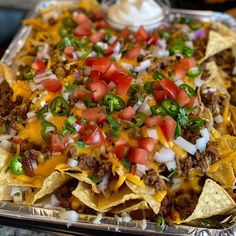 a tray filled with nachos topped with cheese, tomatoes and onions on top of tortilla chips