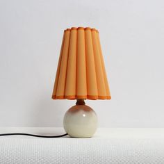 an orange and white lamp sitting on top of a table next to a white wall