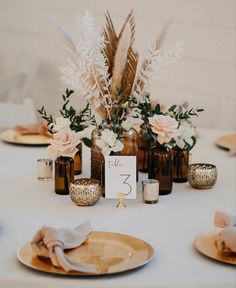 the table is set with gold plates and vases filled with flowers, candles and napkins