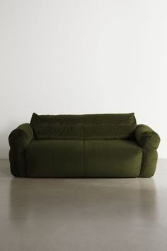 a green couch sitting on top of a cement floor next to a white wall in an empty room