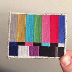 someone is holding up a small patch with different colored squares on the front and back