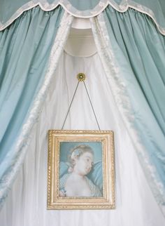 a painting hanging on the wall in front of a blue drapes with a gold frame