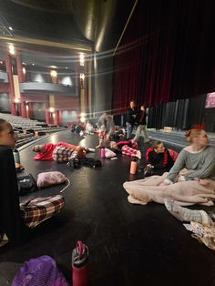 people are sitting on the floor in an empty auditorium with blankets and sleeping bags around them