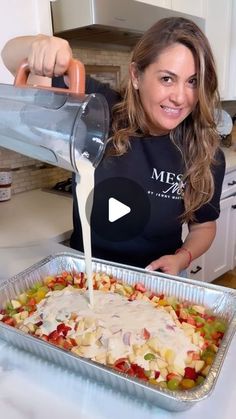 a woman pours dressing into a casserole dish with vegetables and fruit in it