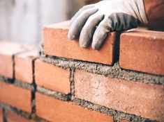 a brick wall being built with gloves on it's arms and hands resting on the bricks