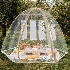 an outdoor dining table under a clear tent in the middle of some bushes and trees