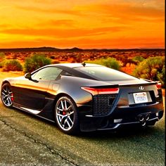 a black sports car parked on the side of a road in front of an orange sky