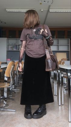 A mid-size person/girl wearing a dark brown thrifted graphic shirt, a black ripped tights shirt under it, a black velvet maxi skirt, black platform dr. Martens and multiple crystal rings and bracelets. 	The person is also wearing multiple silver necklaces, one in form of a moon and another in form of a heart crystal, a black rosary-style necklace and a black lace choker.