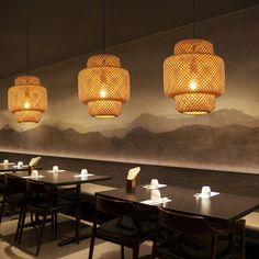 an empty restaurant with wooden tables and hanging lights above them, along with mountains in the background