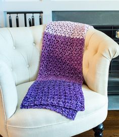 a white chair with a purple crocheted blanket on it and a fireplace in the background