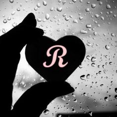 a person holding up a heart with the letter r on it in front of raindrops