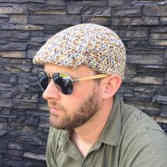 a man wearing sunglasses and a knitted hat looks off into the distance while sitting in front of a stone wall