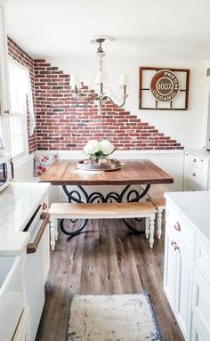 a kitchen with white cabinets and wooden table in front of a red brick wall that has been built into it