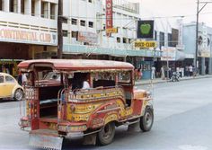 an old fashioned car driving down the street in front of a tall building with shops on it