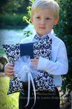 a young boy is holding a pillow and looking at the camera while wearing a black and white outfit