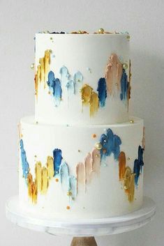 a three tiered white cake with gold and blue icing