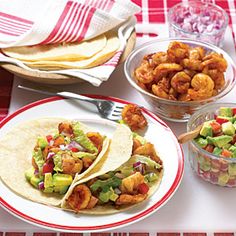 there are two tacos on the table with other food items in bowls and plates