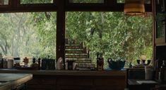 the kitchen counter is covered with dishes and cups in front of an open window that overlooks trees