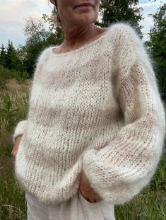 an older woman standing in the grass wearing a white sweater