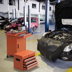 an open car hood in a garage with other cars and tools on the floor next to it