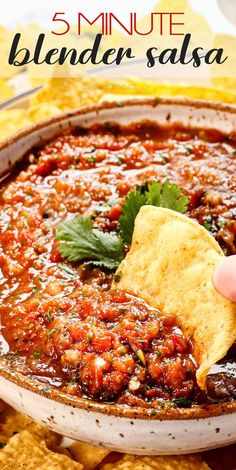 a hand holding a tortilla chip and dipping it into a bowl filled with salsa