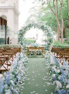 an outdoor wedding ceremony with blue flowers and greenery on the aisle, surrounded by wooden chairs