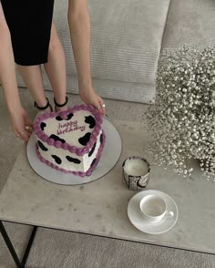 a woman is decorating a heart shaped cake with pink and white frosting on a table