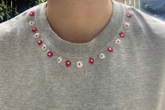 a person wearing a gray shirt with red and white flowers on the collar, standing in front of a fence