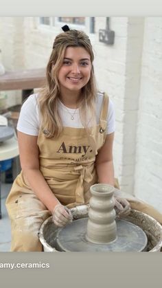 a woman is sitting on a pottery wheel and smiling at the camera while making a vase