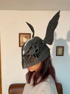 a woman wearing an alien mask with wings on her head, sitting in front of a chair