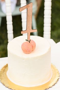 a white cake with a wooden number one on top and two peaches on the side