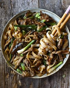 a bowl filled with noodles and meat on top of a wooden table next to chopsticks